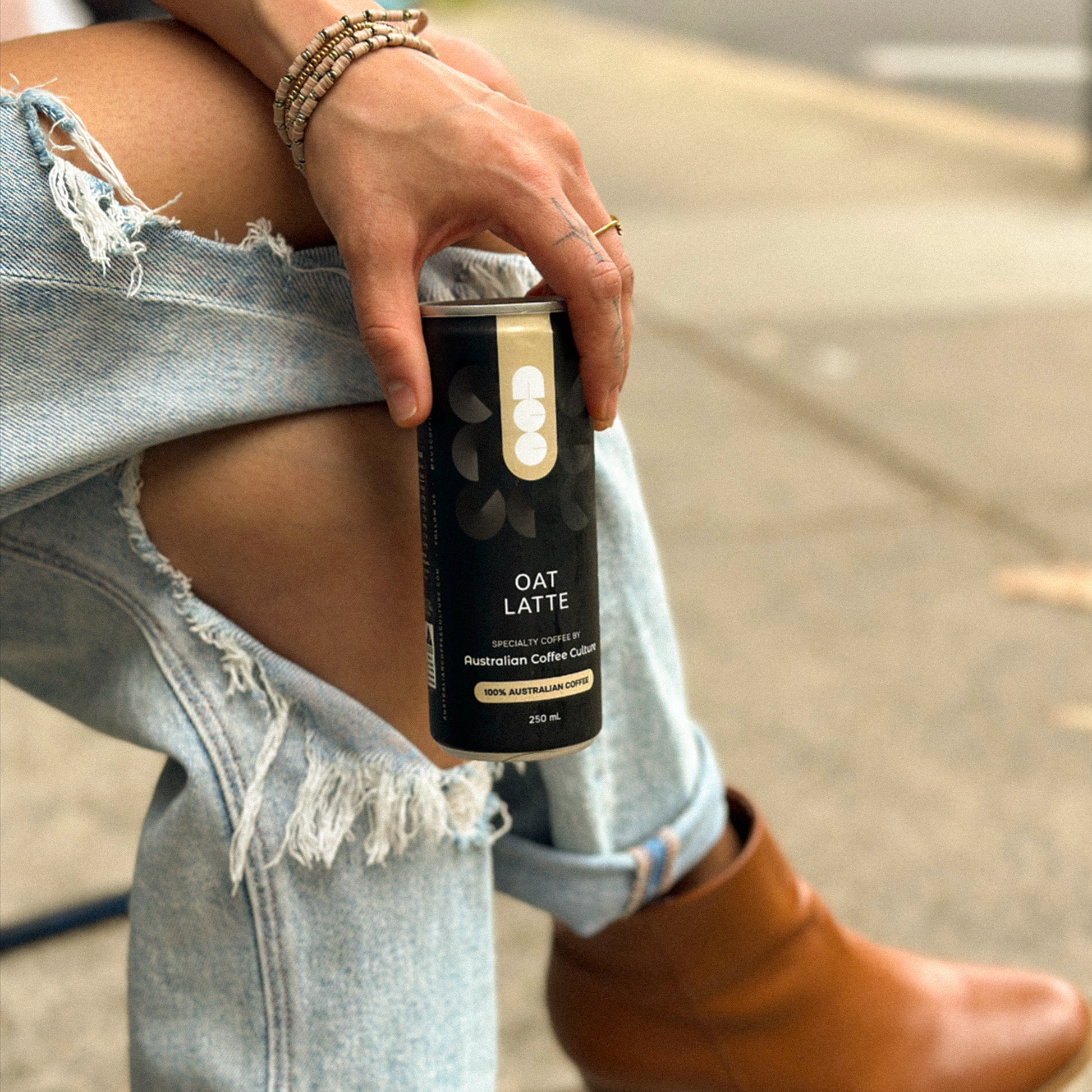Hand holding an Australian Coffee Culture Oat Latte can while seated outdoors